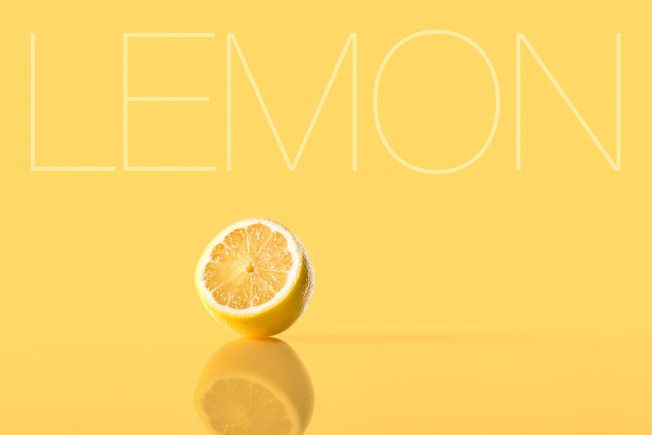 Minimalist commercial photograph of sliced lemon with reflective yellow surface and graphic studio lighting.
